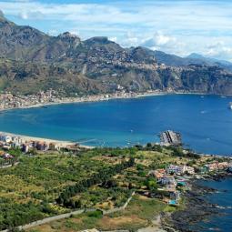 View over Giardini Naxos bay, where cruise ships anchor for shore excursions to Taormina and nearby destinations such as Mount Etna and the Alcantara Valley. The image shows the real cruise gateway to Taormina along Sicily’s Ionian coast.